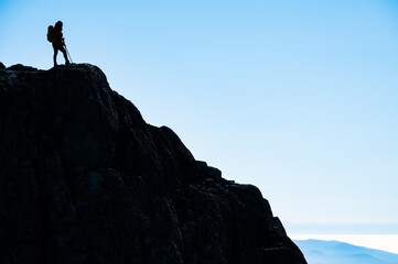 Silhouette of a successful hiker at the edge of the cliff, staring at the horizon