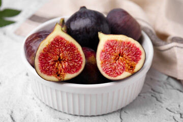 Bowl of tasty ripe figs on white textured table, closeup
