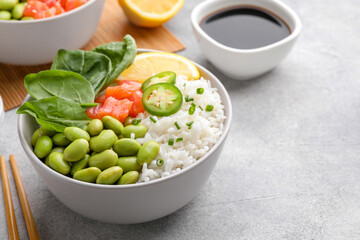 Poke bowl with salmon, edamame beans and rice on light grey table. Space for text