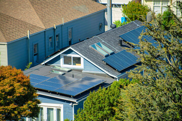 Double gable style rooftop on suburban house with rows of solar pannels and visible windows on gray...