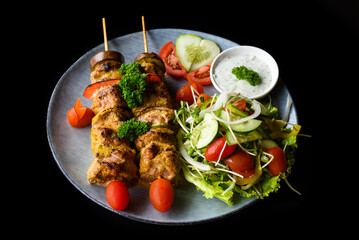 Pork skewers with grilled vegetables served with salad on black background side view