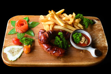 Fried sausages with french fries and spicy sauce on wooden board isolated on black background side view