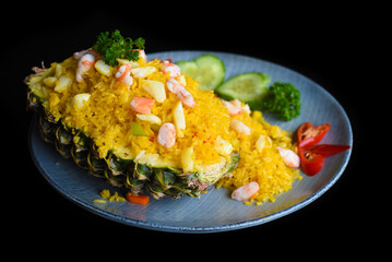 Fried rice with seafood in a pineapple with vegetables on blue plate isolated on black background side view  