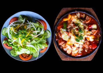 Stewed beef with cheese and vegetables on wooden plate isolated on black background top view
