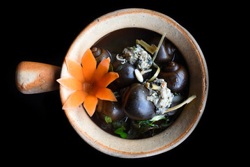 Boiled snails stuffed with pork in a pot with vegetables on black background top view 