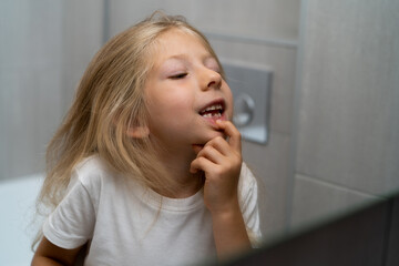 a little girl in the bathroom looks at her teeth in front of a mirror, a little girl has a baby...