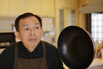 Middle-aged Asian man wearing an apron and frolicking in the kitchen at a good age.