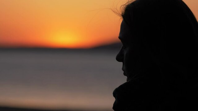 silhouette of pensive woman contemplates the sea at sunset