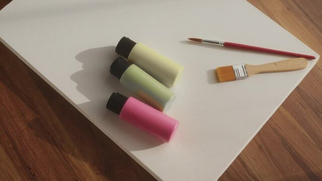 girl put tubes of acrylic paint on table next to empty blank canvas to paint and create masterpiece. Preparation for painting in yellow green and pink colors.