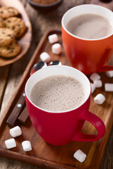 Hot cocoa or hot chocolate in cups with marshmallows and cookies on the side, photographed on wood (Selective Focus, Focus one third into the cocoa's surface)