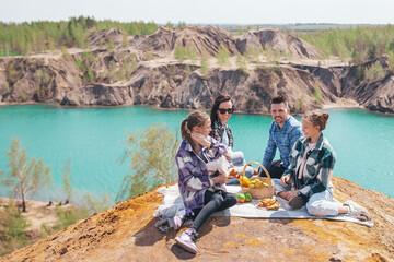 Family of four with dog on picnic after hiking in mountains. Beautiful view of blue lake