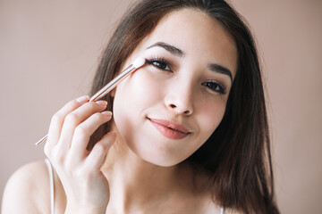 Portrait of young asian woman with makeup brush on beige background