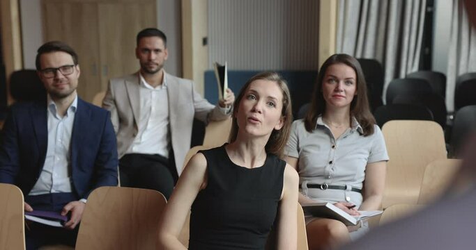 Woman office employee having question about received information, raise arm ask speaker, take part in group corporate seminar sit in conference hall with colleagues participate in educational training