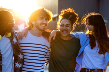 Back lit group of happy and smiling multiracial friends having fun together outdoors in the city during sunset.