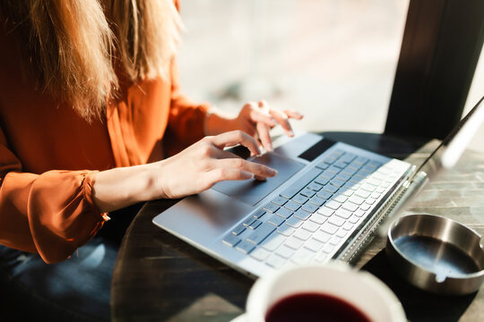 Young businesswoman in a cafe bar or restaurant with bright sunlight. Freelancer girl working on laptop and having tea at a window table. Abstract photo..