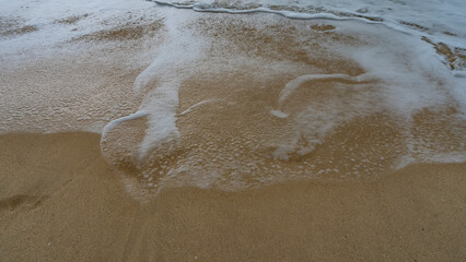 Openwork foam waves. Close-up. Small bubbles are visible on the wet sand of the beach. Seychelles