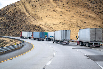 Big rigs semi trucks with loaded semi trailers slowly climbing uphill on the highway road to mountain pass in California - obrazy, fototapety, plakaty