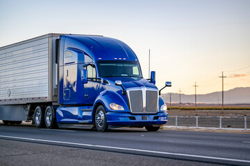Bright blue powerful big rig semi truck transporting cargo in reefer semi trailer driving on the...