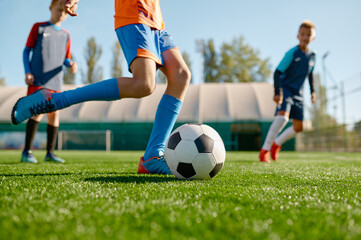 Closeup boy kicking ball while playing football with teammates