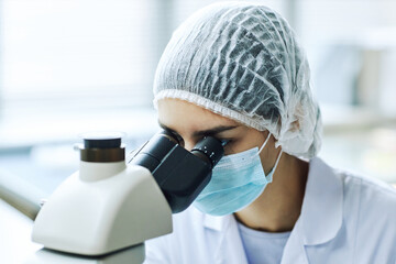 Portrait of female bio engineer looking in microscope while working in scientific laboratory
