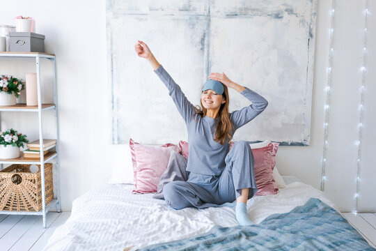 Portrait attractive cute girl enjoying time in post sleep state doing stretching with her hands in blue pajamas with sleep mask on her head. Good afternoon life health concept