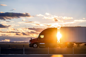 Professional bonnet red big rig semi truck transporting cargo in dry van semi trailer driving on...