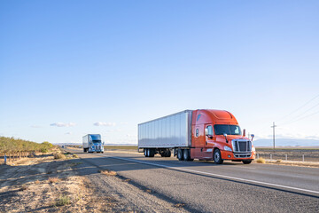 Team of two orange and blue big rigs semi trucks transporting cargo in dry van semi trailers...