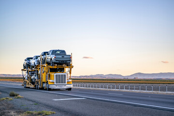 Yellow industrial car hauler big rig semi truck transporting pick up trucks on the two level semi...