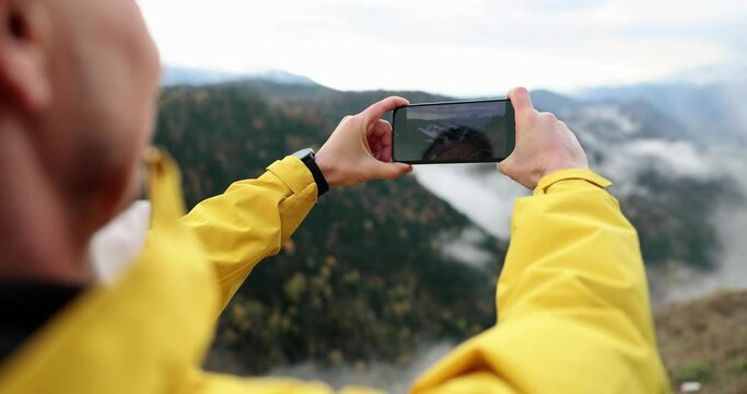 Photographer tourist blogger holds a mobile phone in hands takes pictures on smartphone autumn foggy mountain