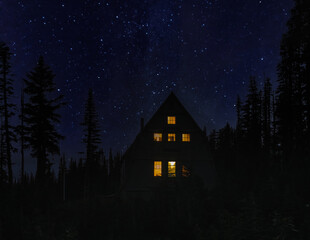 View of cabin in the woods with lit windows on starry night