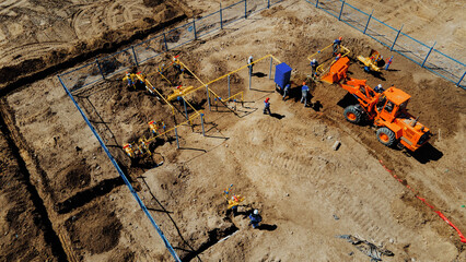 Aerial view excavator and construction workers working on construction site in open field. Pipe...
