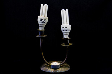 Two non-functional electric globes and a candle on a small stand isolated against a black background