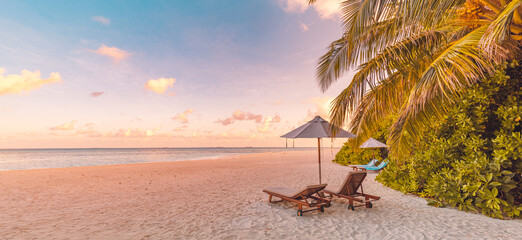 Beautiful panoramic paradise tropical beach sunset as summer island landscape with beds umbrella palm leaves calm sea shore coast. Luxury travel panorama couple destination banner for vacation holiday