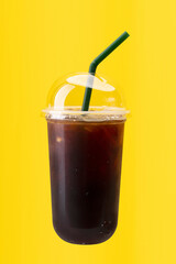 Black ice coffee in plastic cup isolated on yellow background