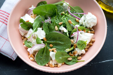 Closeup of salad with spinach leaves, feta cheese, pine nuts and red onion served in a roseate bowl, horizontal shot