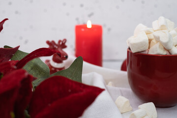 Obraz na płótnie Canvas Red winter marshmallow mug with lighted candle on white background - closeup