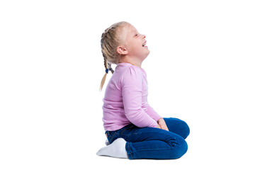 A little girl sits and laughs. Cute blonde child with pigtails in a pink sweater and jeans. Joy, happiness and positivity. Side view. Isolated on white background.