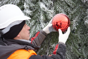 A man decorates a Christmas tree on the street. Working with a Christmas tree outdoors in winter.
