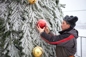 A man decorates a Christmas tree on the street. Working with a Christmas tree outdoors in winter.