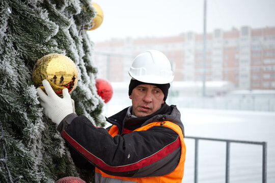 A man decorates a Christmas tree on the street. Working with a Christmas tree outdoors in winter.