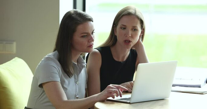 Women colleagues look at laptop screen and discuss on-line project, learn new corporate software or business app. Client make commercial offer, showing online presentation to company client at meeting