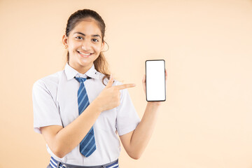 Happy Indian student schoolgirl wearing school uniform holding smart phone and pointing, blank...