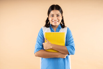 Happy Rural Indian student schoolgirl wearing blue government school uniform holding books and bag...