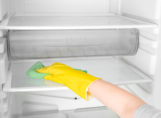 Deep Cleaning service. House cleaning. Washing fridge. Woman hand in yellow rubber protective glove cleaning white open empty refrigerator with green rag. copy space