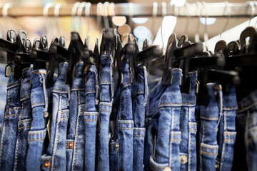Many blue jeans hang on a rack. Close-up of jeans hanging in the store. Jeans or denim pants...