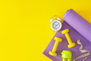 Slimming concept. Flat lay composition of dumbbells bottle of water violet sports mat and alarm...