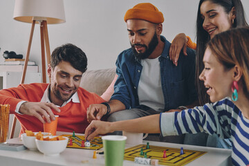Cheerful young people playing board game while enjoying carefree time together