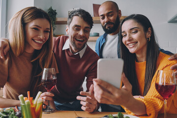 Group of young people looking at smart phone and smiling while enjoying time together