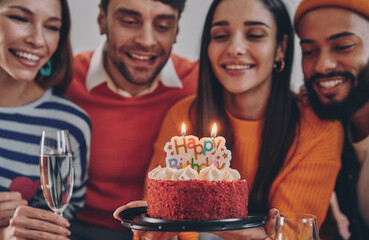 Beautiful young people holding birthday cake and smiling while celebrating together