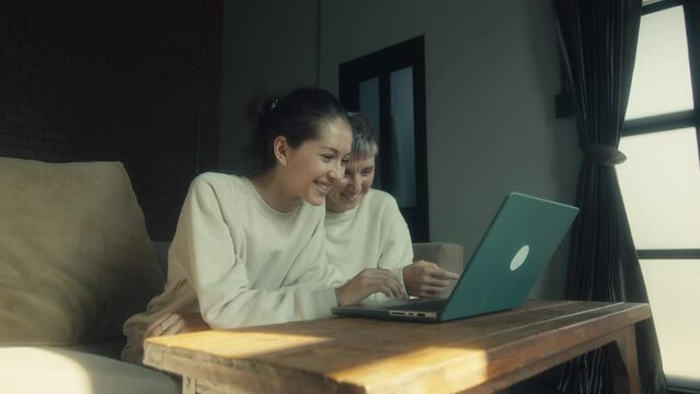 Two young women watching funny videos on their laptops while relaxing together at home